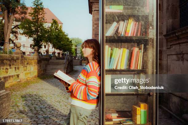 woman reading book from book crossing shelf in the city - woman hand crossed stockfoto's en -beelden