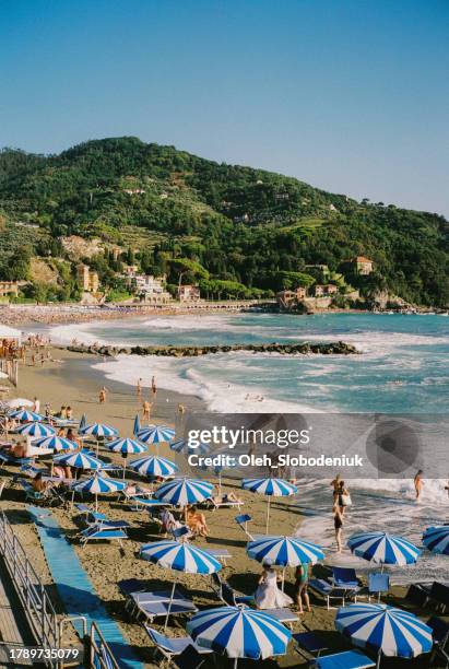scenic view of vernazza beach with blue umbrellas  and chaise lounges - riomaggiore stock pictures, royalty-free photos & images