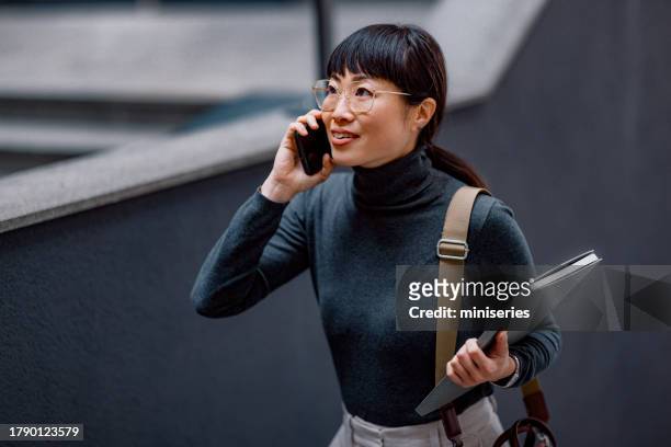 smiling asian businesswoman having a phone call while walking up the stairs going to the office - white collar worker portrait stock pictures, royalty-free photos & images