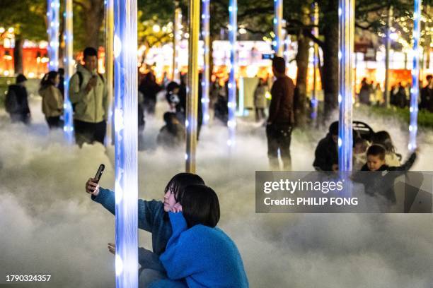 People take pictures among the smoke created by festive light installations at a park in Tokyo's Roppongi district on November 19, 2023.