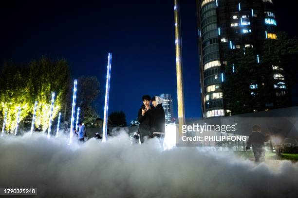 People take pictures among the smoke created by festive light installations at a park in Tokyo's Roppongi district on November 19, 2023.