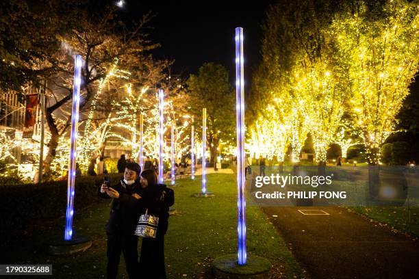 People take pictures in front of illuminated trees at a park in Tokyo's Roppongi district on November 19, 2023.