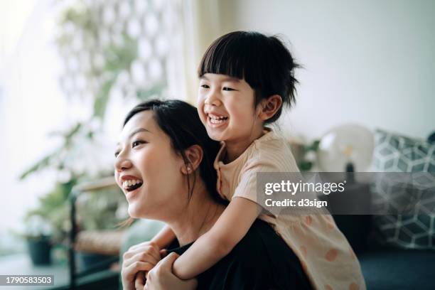 lovely little asian girl embracing her mother while relaxing in the living room at home. sharing mother-daughter bonding moment. love and togetherness concept - mother and daughter kissing stock pictures, royalty-free photos & images