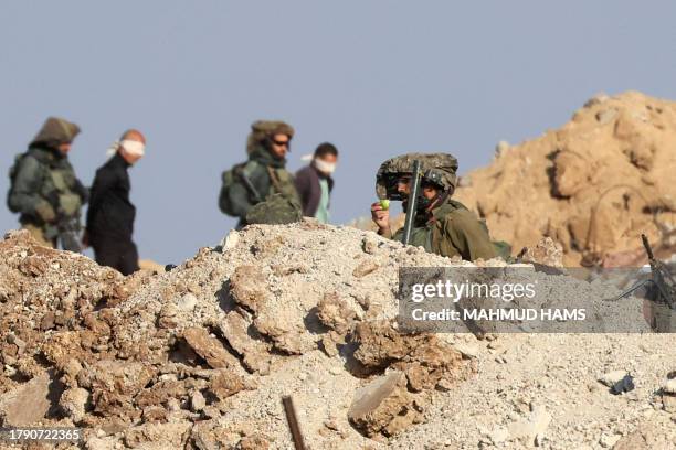 Israeli soldiers detain blindfolded Palestinian men in a military truck while watching Palestinians fleeing the fighting in war-torn Gaza walk by on...