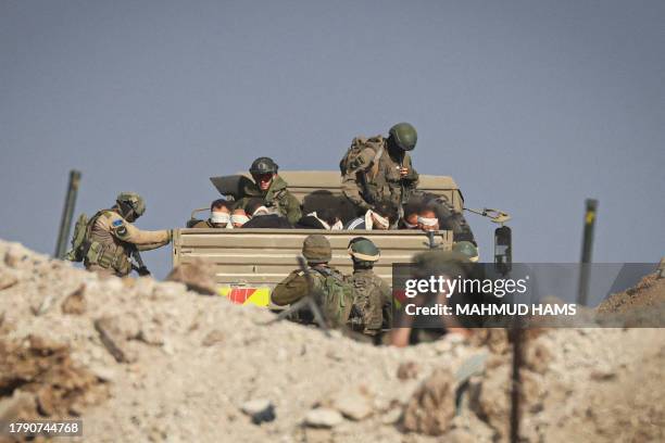 Israeli soldiers detain blindfolded Palestinian men in a military truck while watching Palestinians fleeing the fighting in war-torn Gaza walk by on...