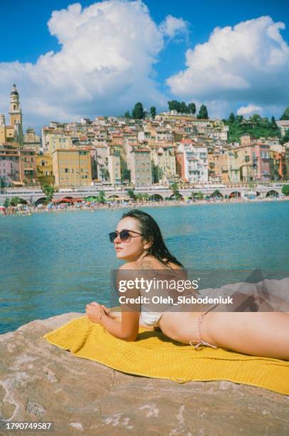 frau mit sonnenbrille sonnt sich am strand von menton - saint tropez stock-fotos und bilder