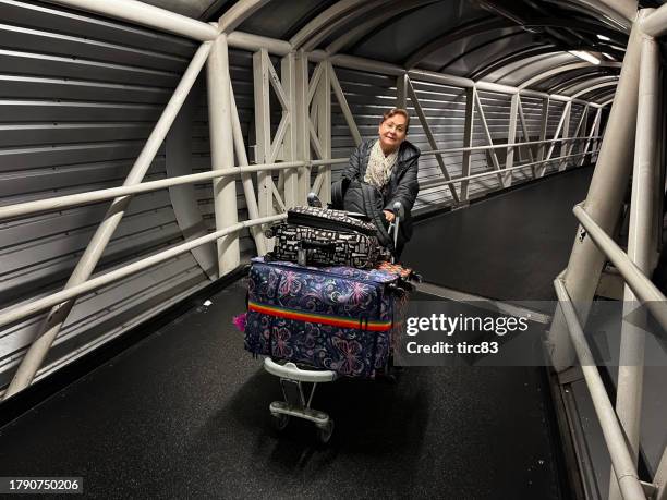 mujer hispana de la tercera edad empujando el carrito de equipaje - carrito-para-equipaje fotografías e imágenes de stock