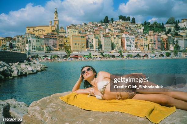 frau mit sonnenbrille sonnt sich am strand von menton - saint tropez stock-fotos und bilder