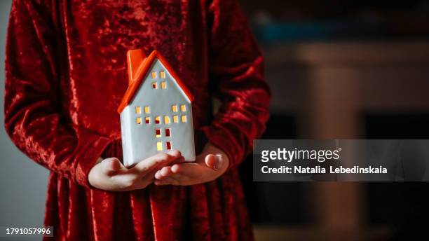 festive illuminance: christmas atmosphere with child and ceramic house lamp in child hands in red velvet. banner and copy space - homeowners decorate their houses for christmas stockfoto's en -beelden