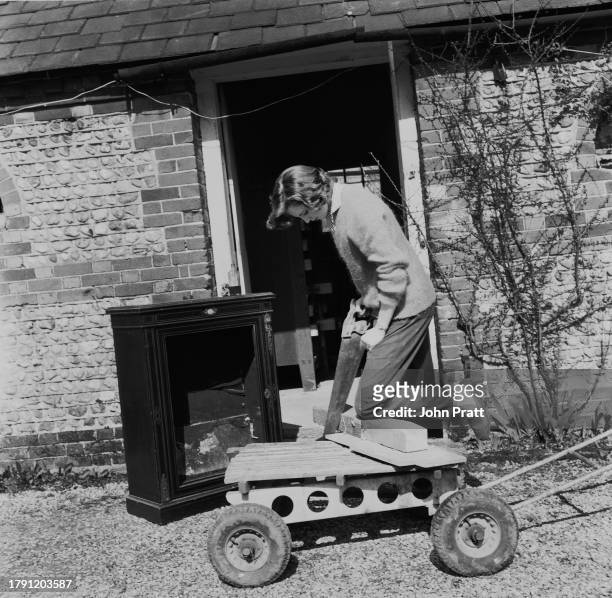 Cabinet maker Julie Powell sawing through a piece of wood outside her workshop in Bosham, Sussex, April 1959.
