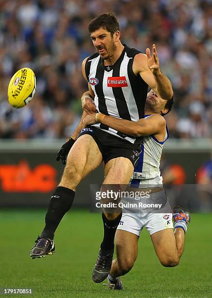 Quinten Lynch of the Magpies kicks whilst being tackled by Lindsay Thomas of the Kangaroos during the round 23 AFL match between the Collingwood...