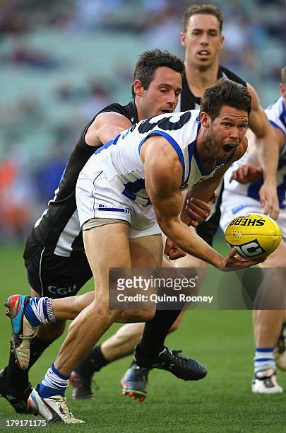 Sam Gibson of the Kangaroos handballs whilst being tackled by Alan Didak of the Magpies during the round 23 AFL match between the Collingwood Magpies...