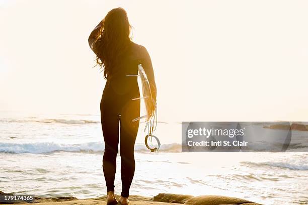 surfer on cliff at sunset looking at waves - neoprenanzug stock-fotos und bilder