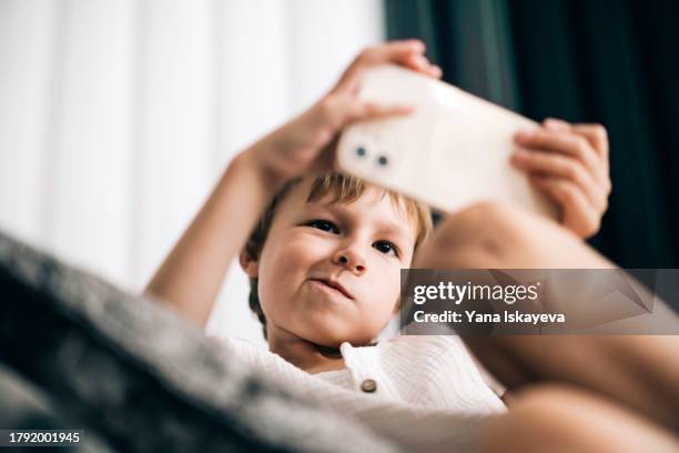 a boy playing games at his smartphone. modern parenthood and the role of gadgets in upbringing process - children screen stock pictures, royalty-free photos & images