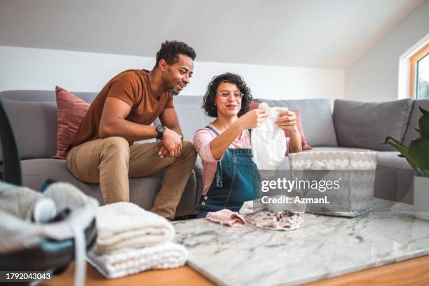 mid adult mixed race pregnant couple getting ready for the arrival of their first kid - baby clothes stock pictures, royalty-free photos & images