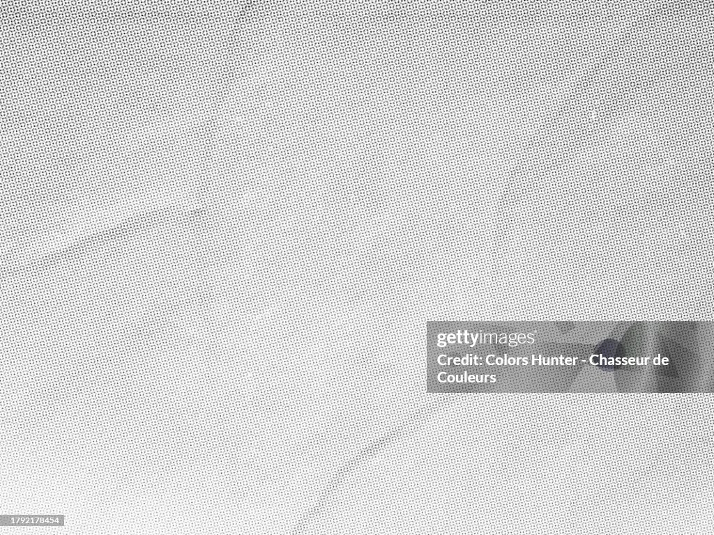 Close-up of a white poster with a mesh of black and grey dots pasted onto a textured wall in Paris, France