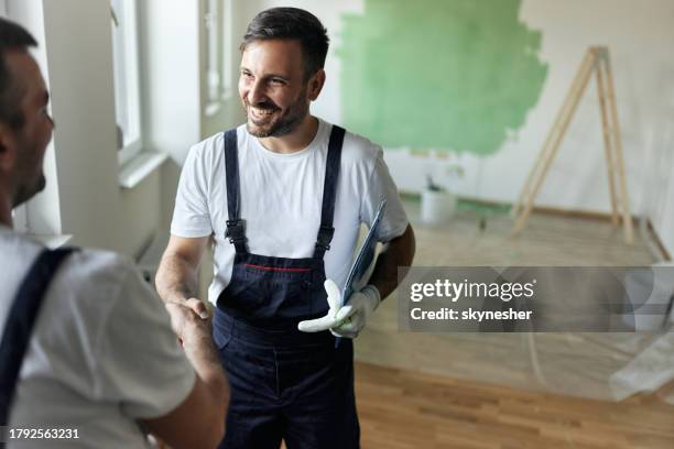 happy house painter shaking hands with his colleague during home renovation process. - huisschilder stockfoto's en -beelden