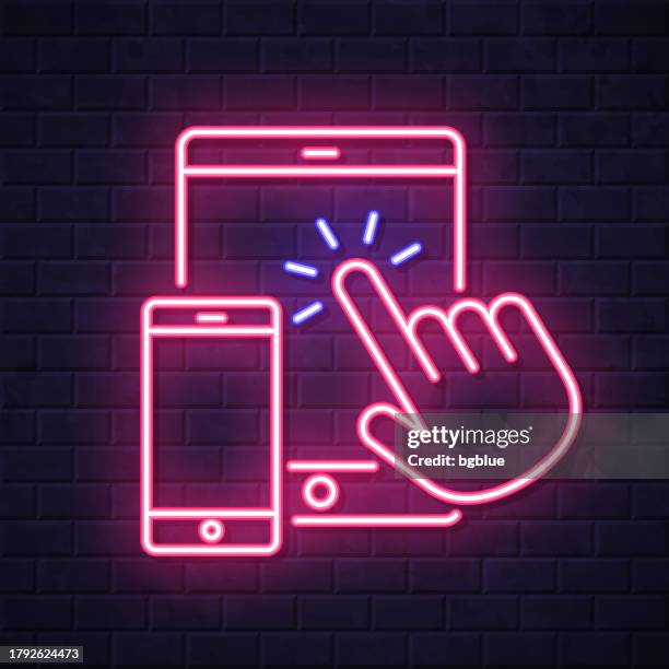 hand touch tablet pc and smartphone. glowing neon icon on brick wall background - touch screen wall stock illustrations