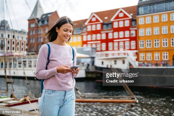 young woman using her phone in nyhavn canal in copenhagen in denmark - copenhagen tourist stock pictures, royalty-free photos & images