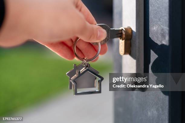 close up of hand with key with a keychain in the shape of a house. mortgage concept - chave imagens e fotografias de stock