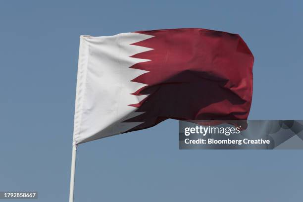 the national flag of qatar flying against a blue sky - bandeira do qatar imagens e fotografias de stock