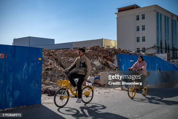 People cycle past demolished buildings in Yuxinzhuang village in Beijing, China, on Friday, Nov. 17, 2023. China home prices fell the most in eight...