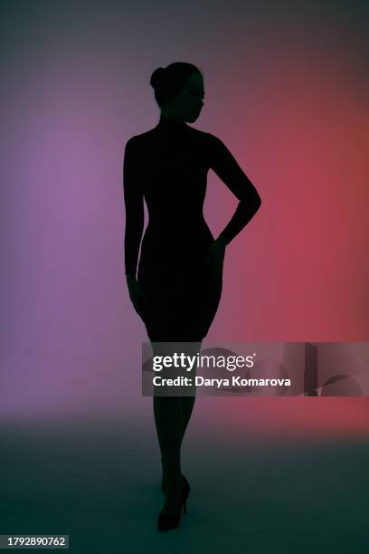 a beautiful woman in a tight black dress on a colored background. silhouette of a woman against a gradient background. - woman body contour standing stockfoto's en -beelden