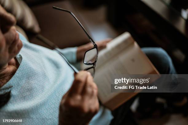 donna anziana che mette gli occhiali per preparare un libro a casa - occhiali da lettura foto e immagini stock
