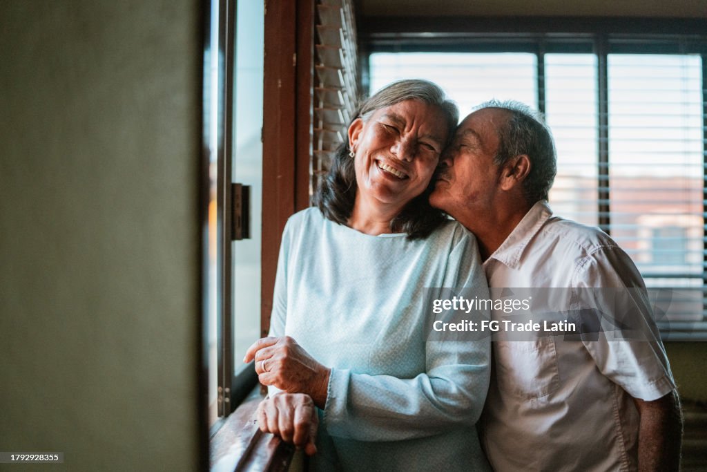 Senior man kissing his wife's cheek in the living room at home