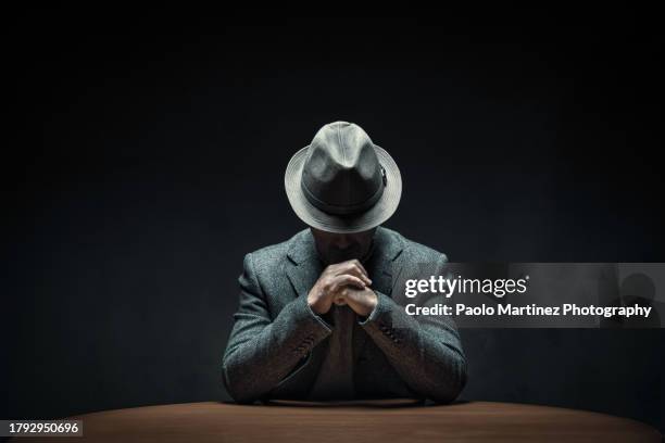 mystery man sitting at table in a dark room - investigatore foto e immagini stock