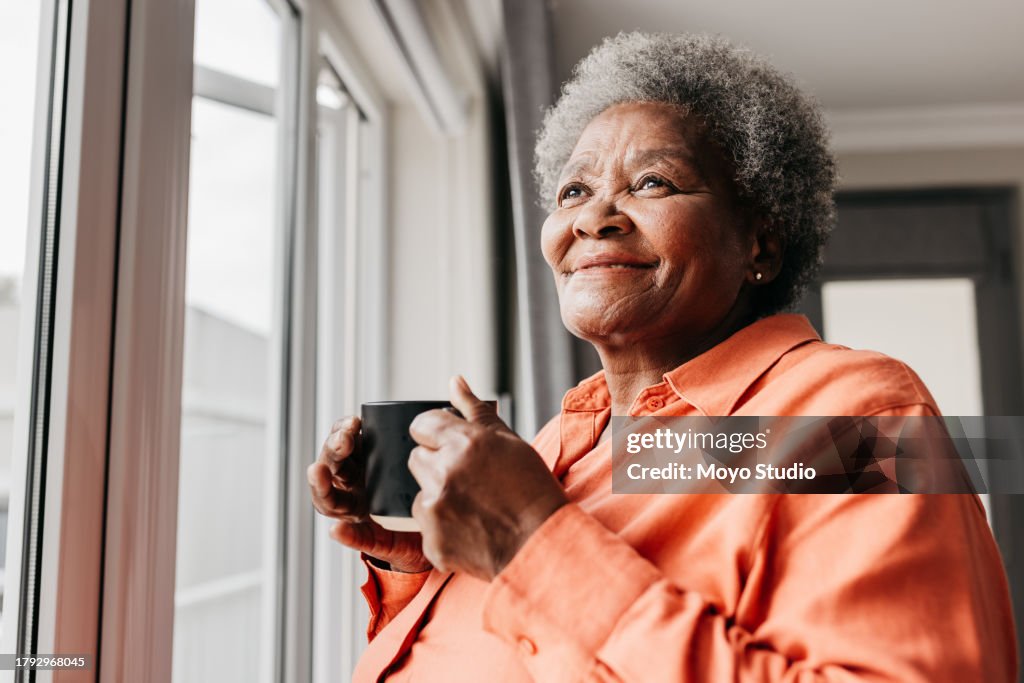 Gros plan d’une femme âgée tenant une tasse, souriant à côté de la fenêtre