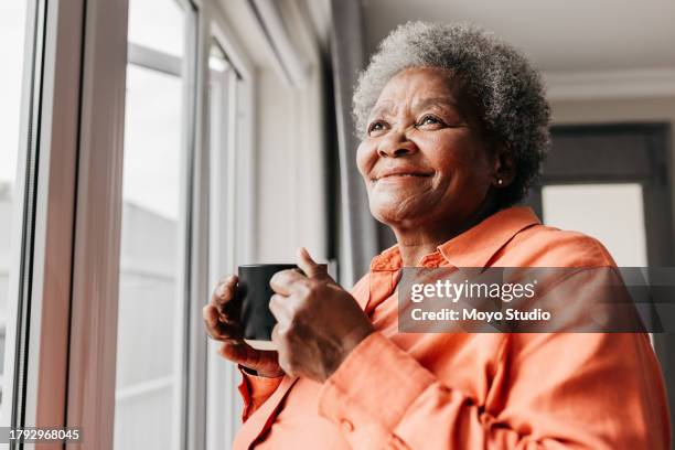 gros plan d’une femme âgée tenant une tasse, souriant à côté de la fenêtre - femmes seniors photos et images de collection