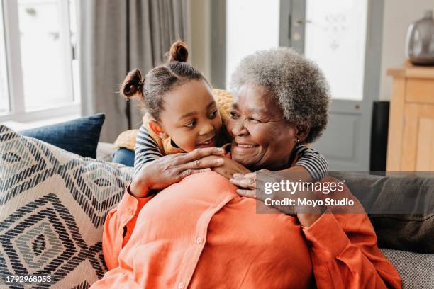 front view of grandmother and granddaughter smiling at each other on sofa - een dag uit het leven serie stockfoto's en -beelden