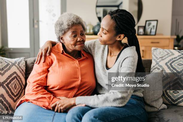 giovane donna che abbraccia e conforta la madre sul divano a casa - accudire foto e immagini stock