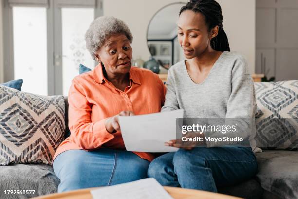 young woman reading financial document in her hand to mother on sofa - family financial planning stock pictures, royalty-free photos & images