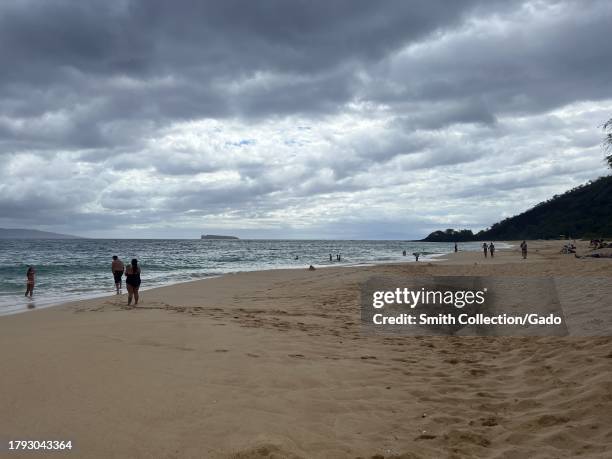 Group of people enjoying a sunny day on Makena Alanui beach, surrounded by coastal landforms, under a sky filled with cumulus clouds, Kanahena, Maui...