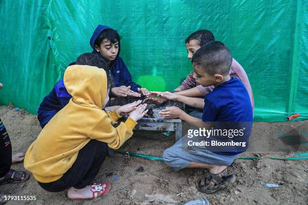 Children warm themselves around a brazier in a camp for displaced Palestinians near the Shuhada Al-Aqsa hospital in Deir al-Balah, Gaza, on Monday,...