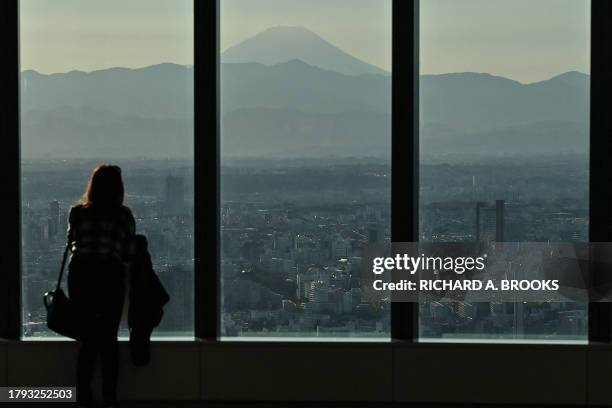 Woman looks out towards the western suburbs of the city as Mount Fuji looms in the distance, as seen from the viewing deck of "Azabudai Hills" - the...