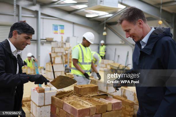 Britain's Prime Minister Rishi Sunak and Britain's Chancellor of the Exchequer Jeremy Hunt learn how to lay bricks during a visit to a college in...