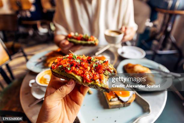 man eating avocado toast with tomato at the cafe, personal perspective view - avocado toast stock pictures, royalty-free photos & images