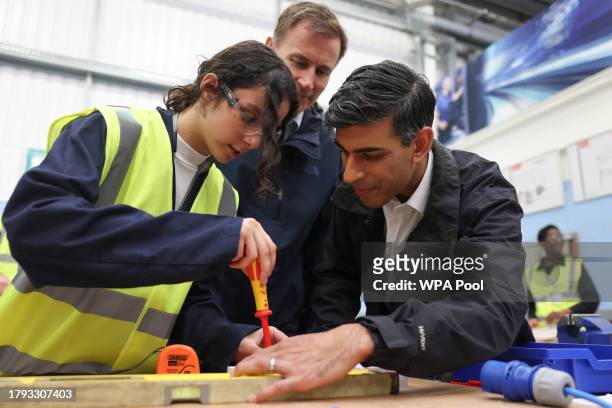 Britain's Prime Minister Rishi Sunak and Britain's Chancellor of the Exchequer Jeremy Hunt assist an apprentice doing electrical work during a visit...