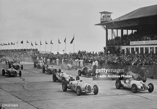 Spectators in the grandstand look on as pole sitter Bernd Rosemeyer from Germany, driver of the Auto Union AG Auto Union Type C and compatriots...