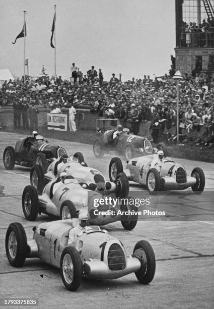 Spectators in the grandstand look on as pole sitter Bernd Rosemeyer from Germany, driver of the Auto Union AG Auto Union Type C and compatriot...