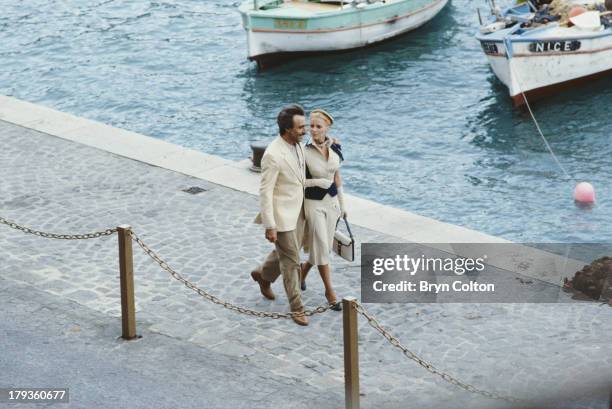 American Hollywood actress Cheryl Ladd, playing Grace Kelly, and actor Alejandro Rey, playing Oleg Cassini, walk arm in arm along a quayside in...