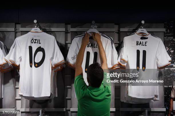 An employee displays new Gareth Bale Real Madrid shirts at the Real Madrid Oficcial Store alongside Mesut Ozil's shirt on the day Gareth Bale is...