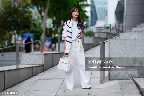 Heart Evangelista wears a dark navy blue and white wool knit pullover from Joshua's x Smiley, a white t-shirt from Frankie Shop, a white leather...