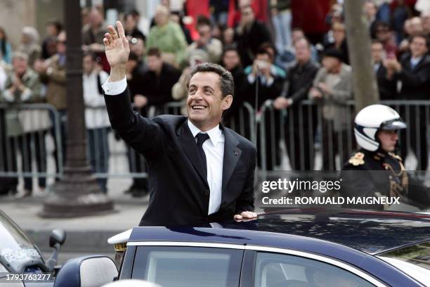 French President Nicolas Sarkozy waves from his car as he is driven up the Champs Elysees avenue in Paris in an open-top car, escorted by the mounted...