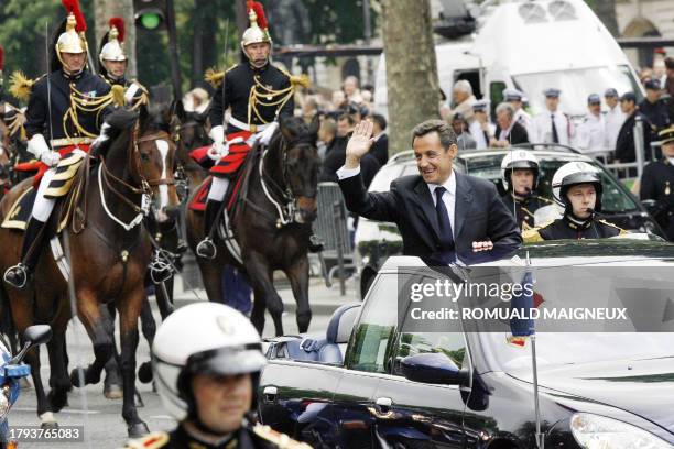 French President Nicolas Sarkozy waves from his car as he is driven up the Champs Elysees avenue in Paris in an open-top car, escorted by the mounted...