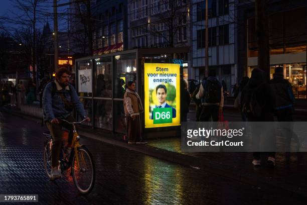 Woman checks her phone as she waits at a bus stop next to a campaign poster for the Democrats 66 party featuring a picture of party leader Rob Jetten...