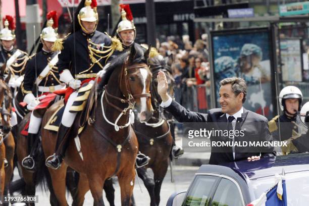 French President Nicolas Sarkozy waves from his car as he is driven up the Champs Elysees avenue in Paris in an open-top car, escorted by the mounted...